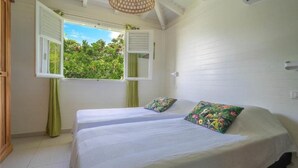 A room with two beds, a window with open shutters, and a ceiling fan.