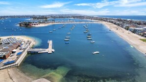 Vista aérea de un puerto deportivo con numerosas embarcaciones amarradas, una playa de arena y un cielo azul despejado.