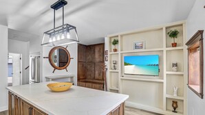 Una cocina con una isla grande, armarios de madera, un espejo redondo y un televisor instalado en la pared.