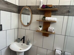 A bathroom with a white sink, a mirror, and wooden shelves holding towels and toiletries.