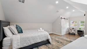 A bedroom with a bed, a chair, a desk, and a window.