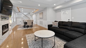 A spacious living area with a fireplace, a dining table with chairs, a sofa, and a staircase leading to an upper level.