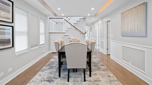 A hallway with a dining area featuring a table and chairs, a staircase, and artwork on the walls.