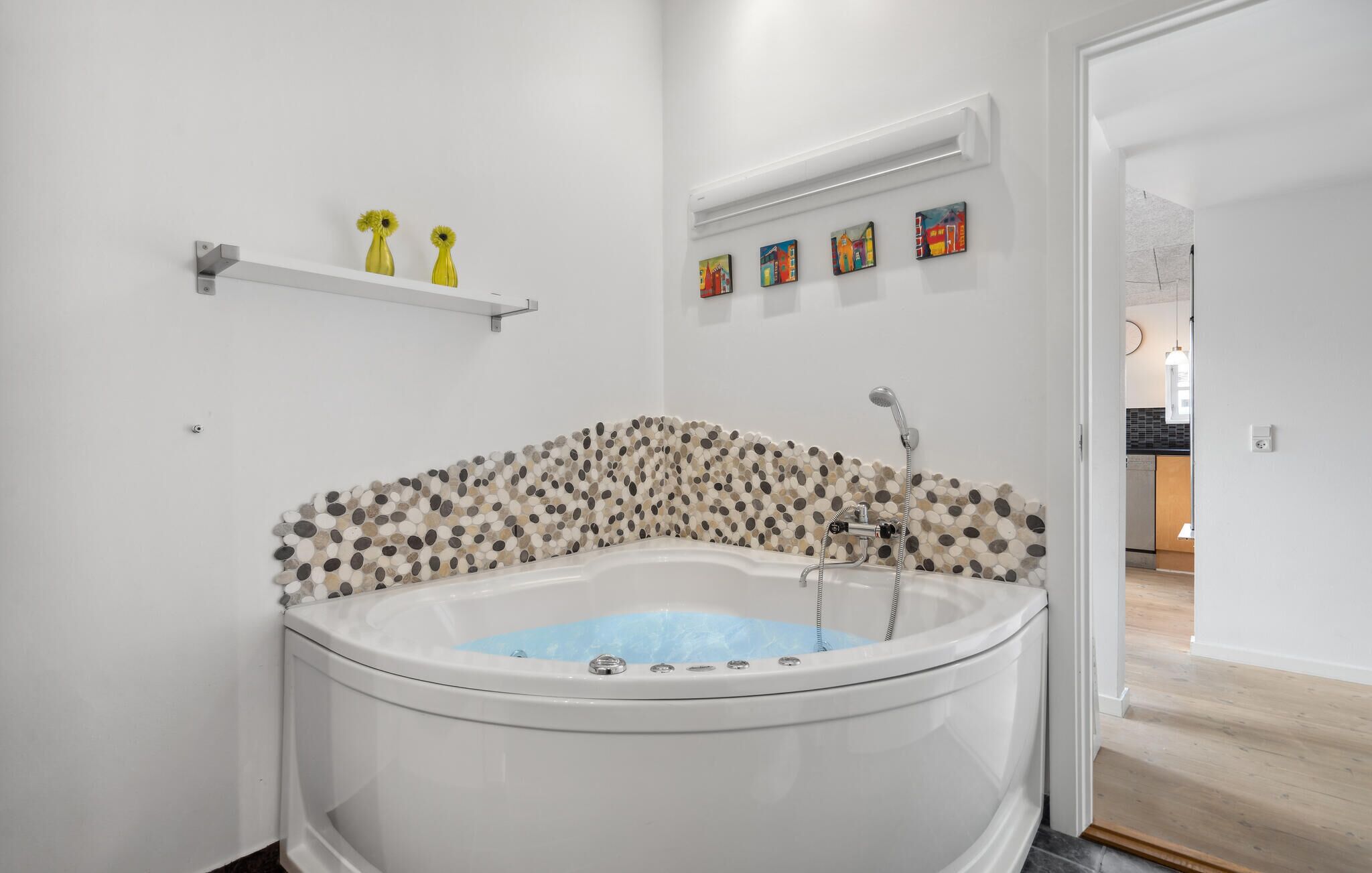 Een moderne badkamer met een vrijstaand bad, een douche en een wand betegeld met mozaïek. Boven het bad staat een plank met drie gele vazen.