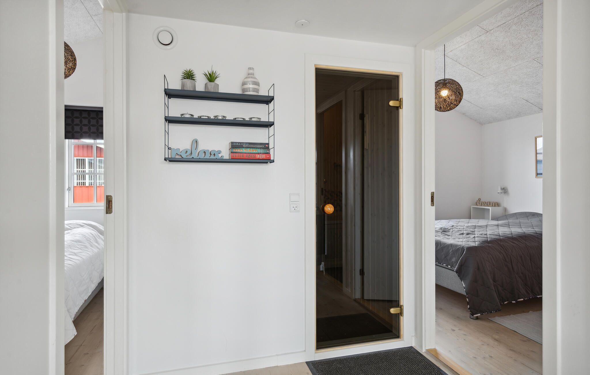 Een slaapkamer met een bed, een nachtkastje, een wandplank met boeken en decoratieve objecten, en een deur die naar een andere kamer leidt.