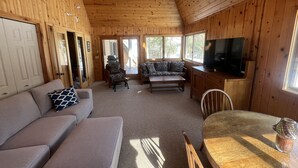 Ein gemütliches Blockhaus-Interieur mit einer Couch, einem Sessel und einem Esstisch.
