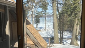 Blick aus einem Haus auf eine verschneite Terrasse mit einer Holztreppe zu einem Terrassenbereich.