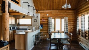 A log cabin interior with a kitchen, dining area, and a loft space.