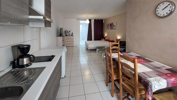 Cocina compacta con cafetera, estufa y pileta. Hay un comedor con mesa y sillas, y una cama al fondo.