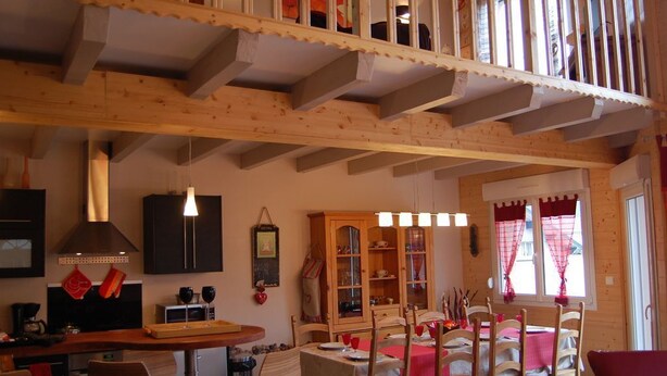 Ein gemütlicher Essbereich mit Holztisch und -stühlen, im Hintergrund eine Küche und ein Balkon mit Geländer.