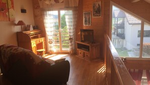 Ein gemütliches Wohnzimmer mit einer Couch, einem Fernseher auf einem Holzboden und einem großen Fenster mit Vorhängen.