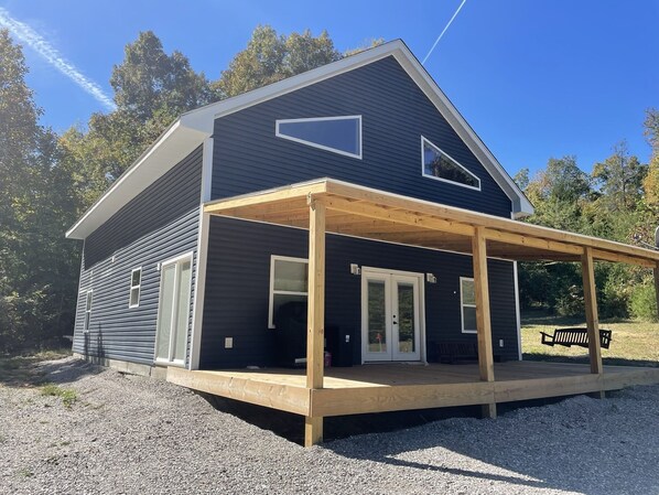 A two-story house with a dark exterior, a wooden deck, and a covered porch.