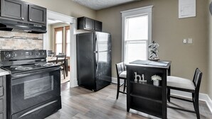 A kitchen with a black stove, refrigerator, and dark wooden cabinets. There is a window with blinds and a small table with chairs. - Cheerful 4-Bedroom home in Midtown Omaha (Omaha)