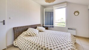 Een slaapkamer met een bed, een raam met gordijnen, een spiegel aan de muur en een plafondlamp.