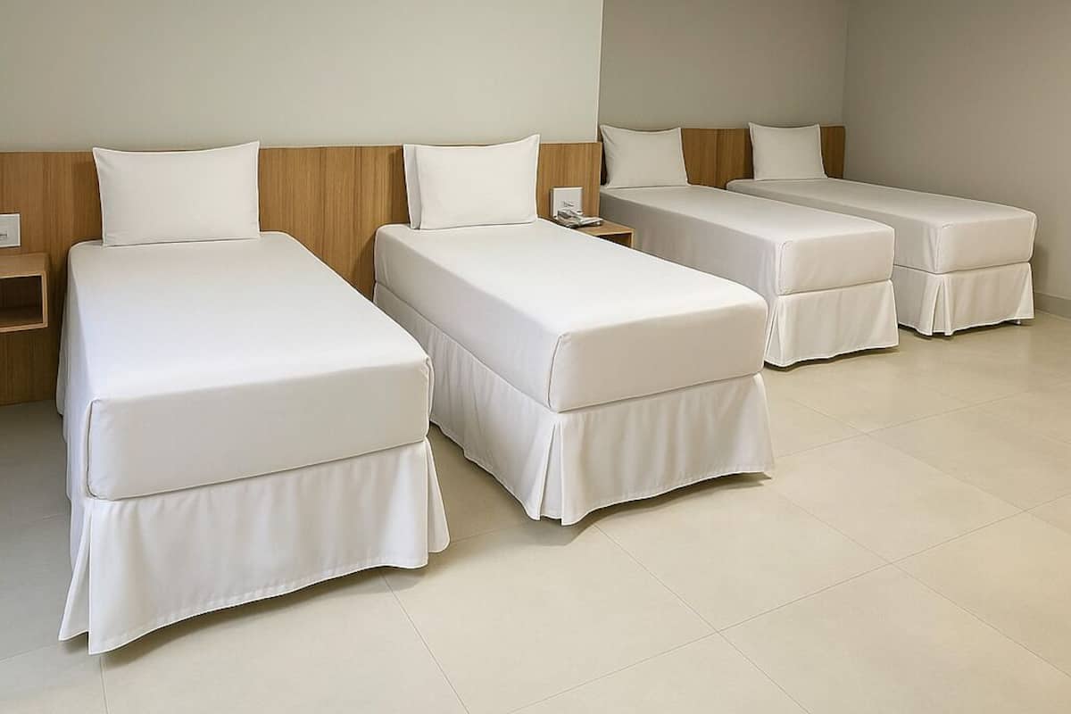 A hotel room with three single beds, a wooden headboard, a nightstand, and a ceiling light.