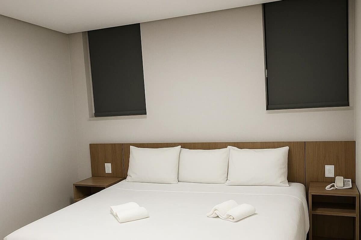 A hotel room with a large bed, two bedside tables, a flat-screen TV on the wall, and a ceiling light.