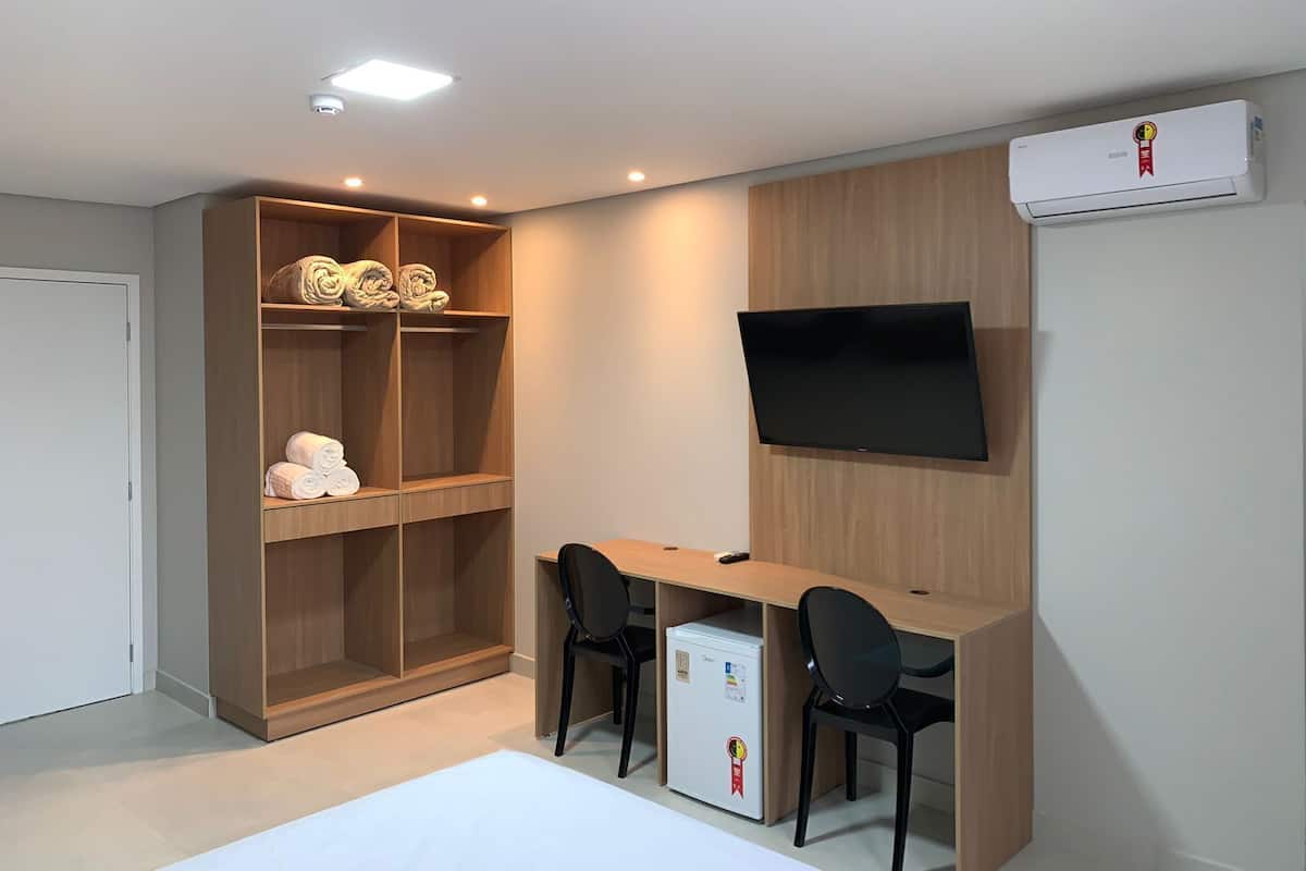 A modern room with a built-in TV, a wooden desk, two chairs, a mini-fridge, and a storage unit with shelves.