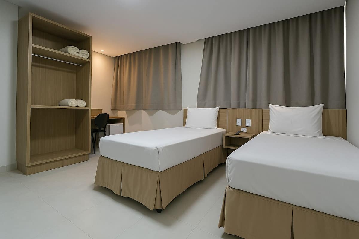 A hotel room with two beds, a wooden wardrobe, a desk, and a chair.