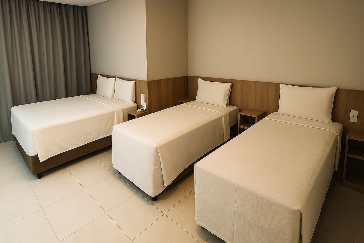 A hotel room with three single beds, wooden headboards, and bedside tables with lamps.