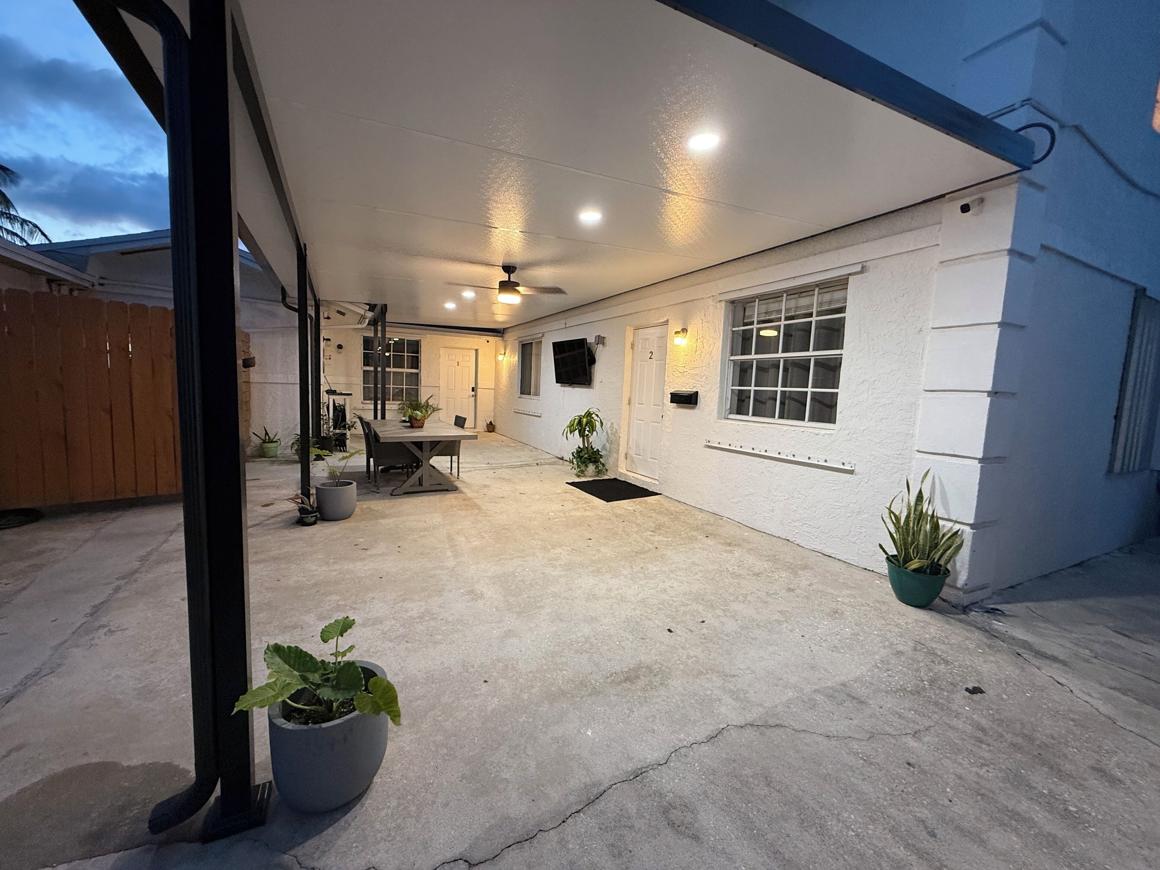 Un patio couvert avec un sol en béton, une table, des chaises et des plantes en pot.