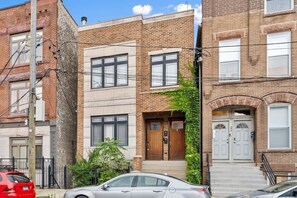 A two-story brick building with a central entrance, a small porch, and a car parked in front.