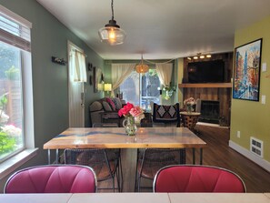 A dining area with a wooden table, red chairs, a hanging light fixture, a sofa, and a TV mounted on the wall.