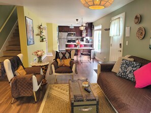 A living room with a sofa, chairs, a coffee table, and a kitchen in the background.