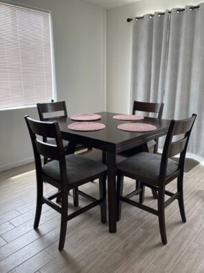 Un comedor con una mesa de madera oscura y cuatro sillas, cada una con un mantel individual rosa.