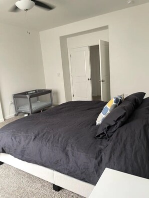 Un dormitorio con una cama grande, un ventilador de techo, una puerta blanca y una pequeña mesa con un colchón encima.