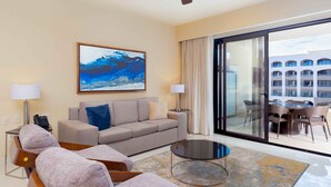 A modern hotel room with a grey sofa, a round coffee table, and a large window with a view of a building. - Spacious Two Bedroom Suite....Amazing Pools including a Lazy River (San José del Cabo)