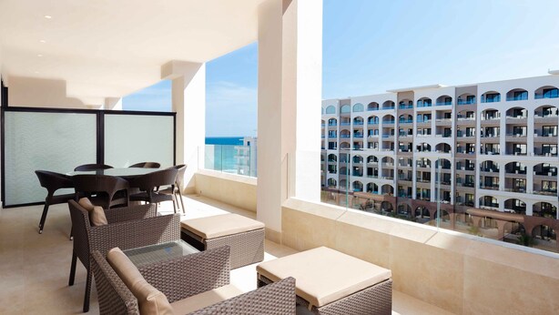 A balcony with wicker furniture, a glass table, and a view of a hotel building. - Spacious Two Bedroom Suite....Amazing Pools including a Lazy River (San José del Cabo)