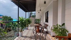 Un espace extérieur abrité, aménagé avec des sièges, un sol décoré, des plantes en pot et un escalier menant à un niveau supérieur.