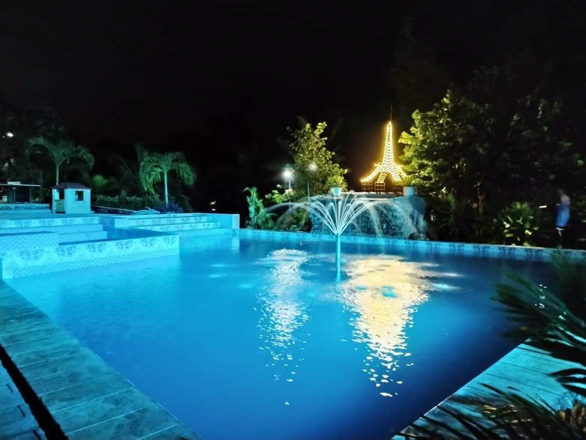 Piscina nocturna con una fuente y una réplica iluminada de la Torre Eiffel al fondo.