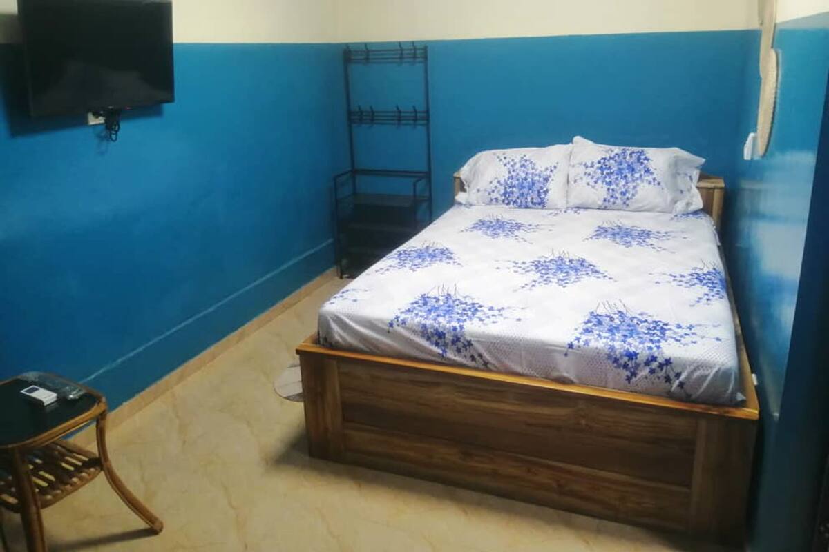 Un dormitorio con una cama, un televisor montado en la pared y una silla.