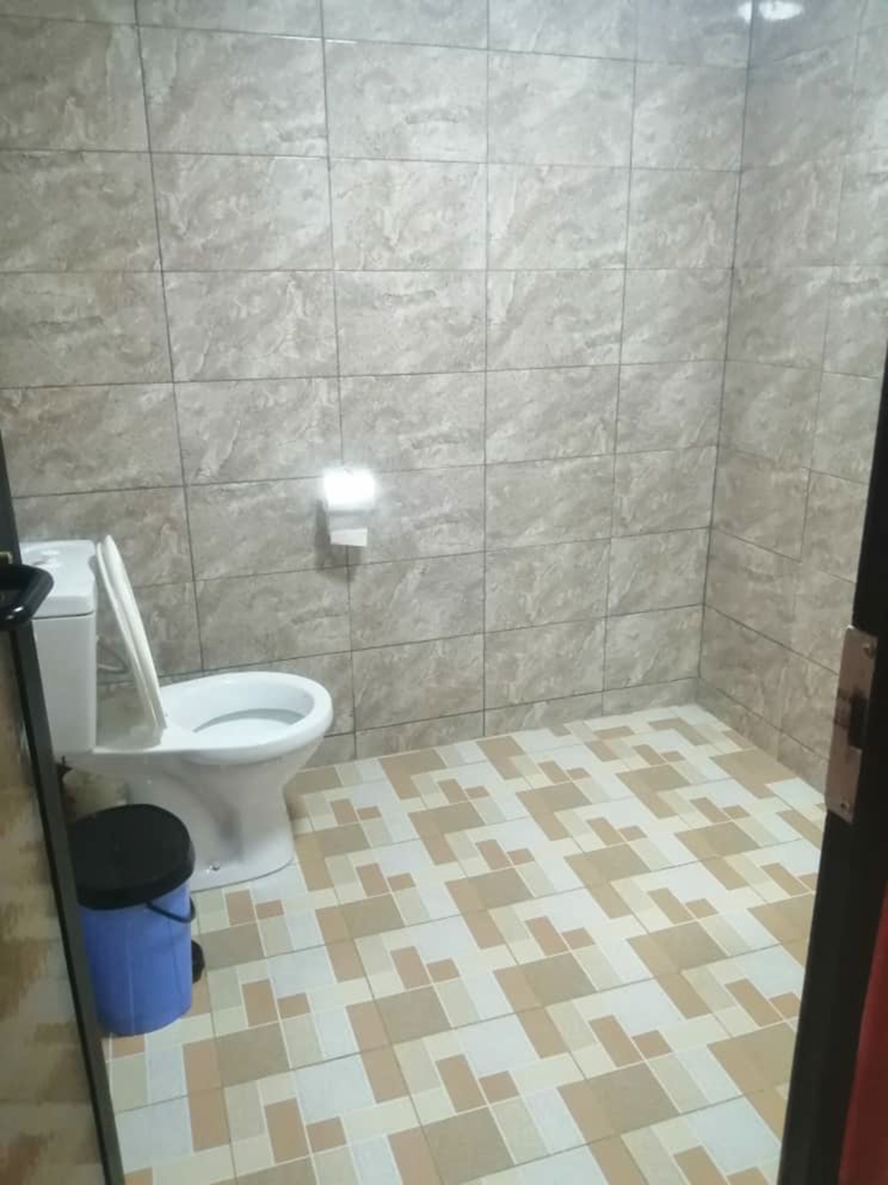 Un baño con inodoro, un cubo de basura azul y baldosas de suelo estampadas.