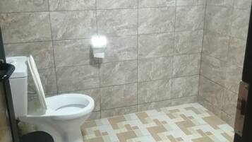 Un baño con inodoro, un cubo de basura azul y baldosas de suelo estampadas.