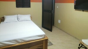 Un dormitorio con cama, cabecera de madera, televisor montado en la pared y aire acondicionado.