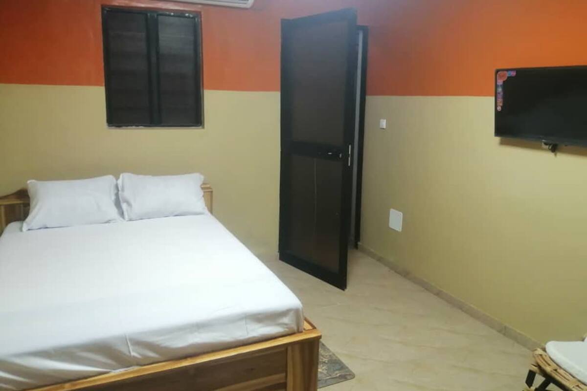 Un dormitorio con cama, cabecera de madera, televisor montado en la pared y aire acondicionado.