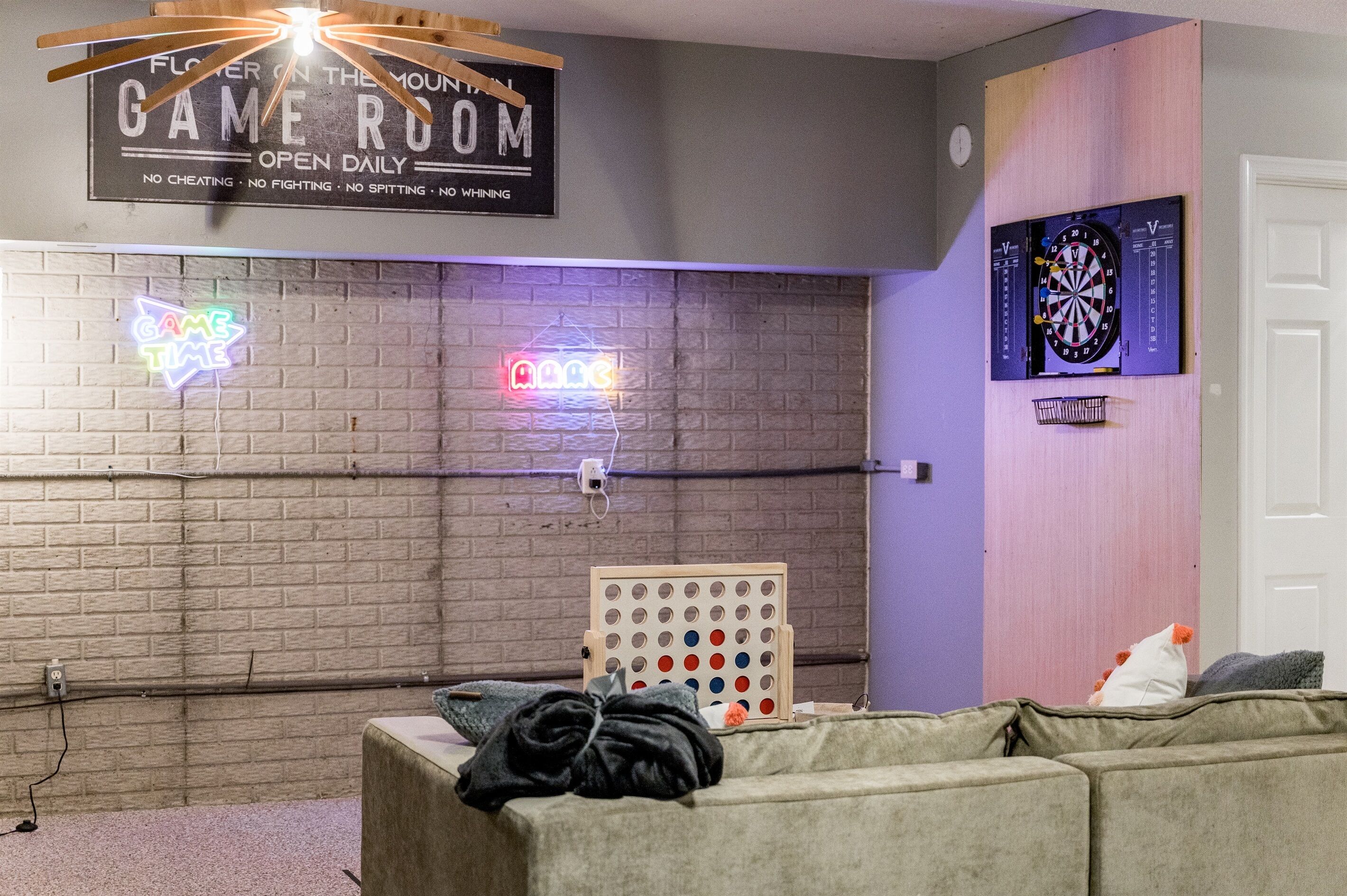 A room with a dartboard, a neon sign, and a sign that reads "GAME ROOM OPEN DAILY."