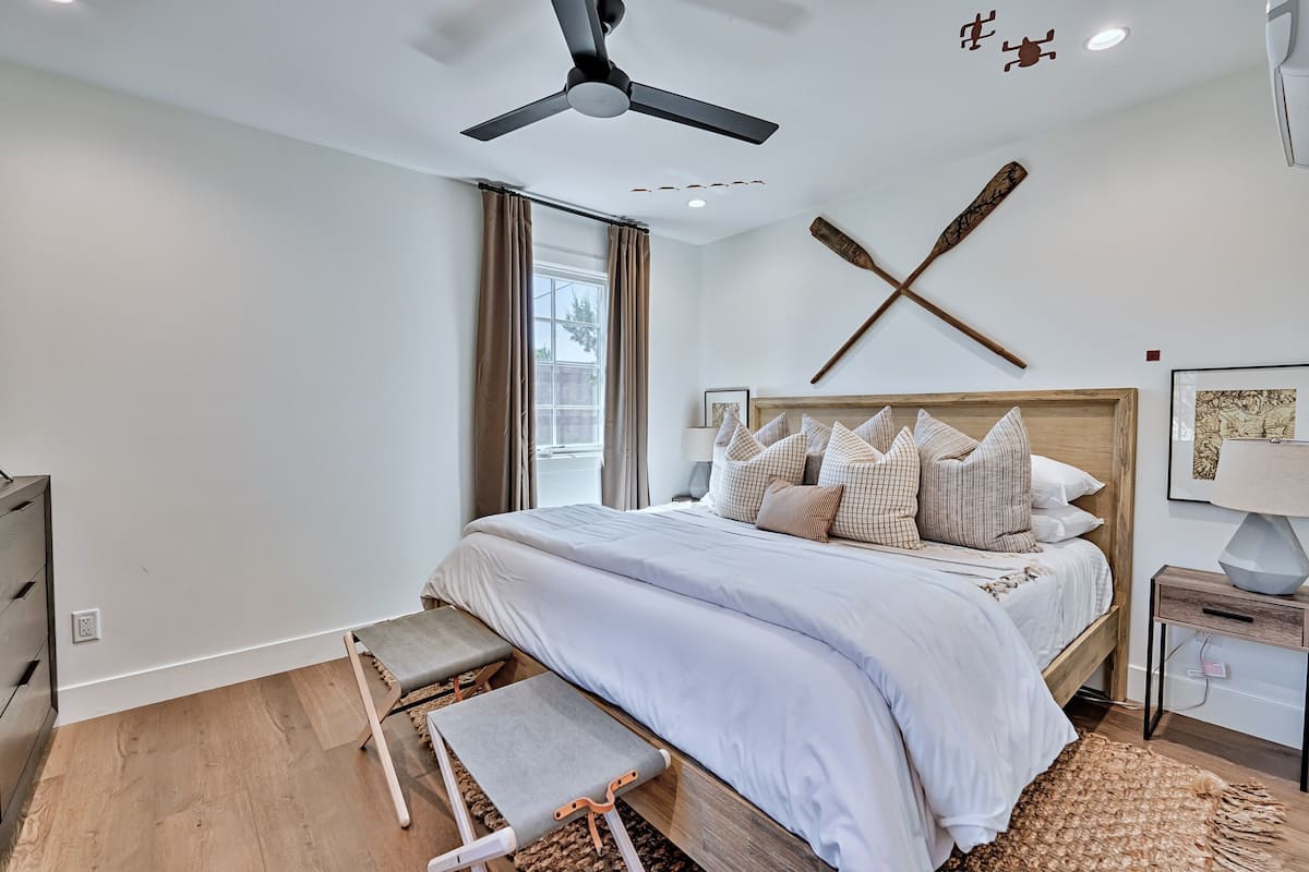 A modern bedroom with a large bed, a ceiling fan, and a wooden wall decoration.