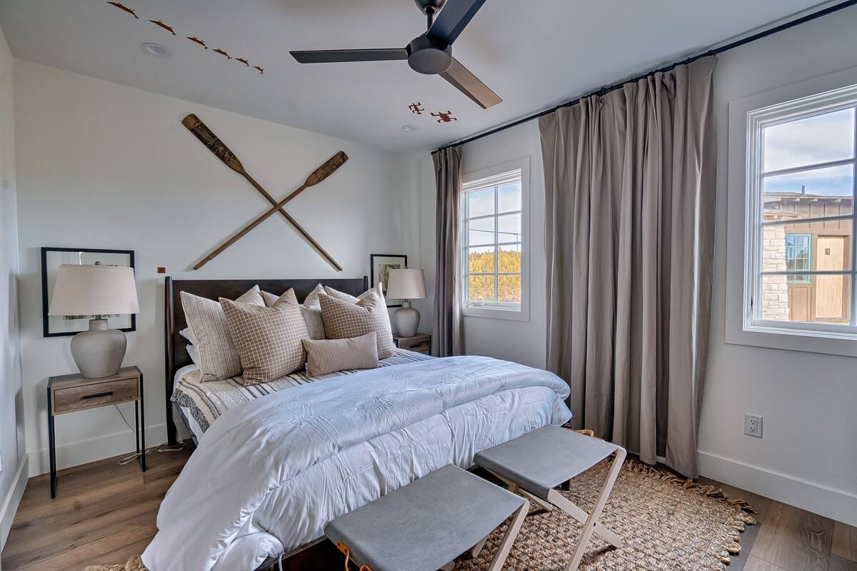 A bedroom with a large bed, two bedside tables, a ceiling fan, and a view of the outside through a window.