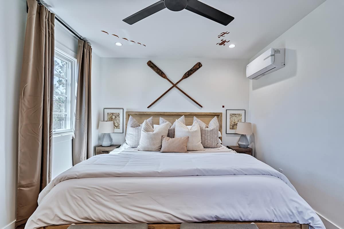 A bedroom with a bed, a ceiling fan, an air conditioning unit, and a window with curtains.