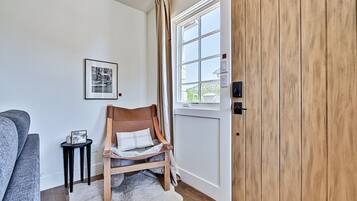 A room with a wooden wardrobe, a grey sofa, a small black side table with a framed picture, and a fluffy white rug.