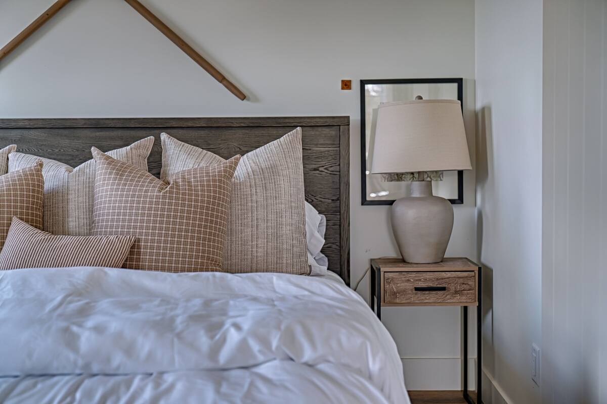 A neatly made bed with a wooden headboard, a bedside table with a lamp, and a framed picture on the wall.