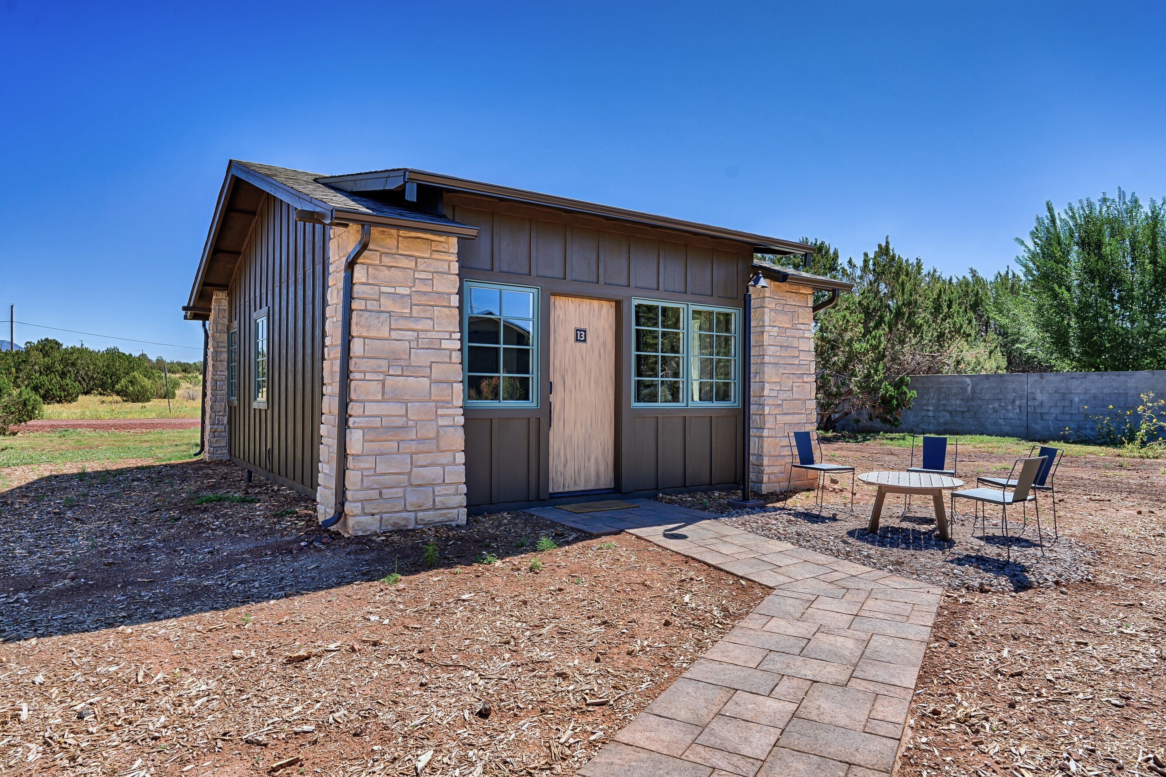 A small, single-story building with a brick exterior and large windows. There is a paved patio area with a table and chairs.