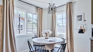 A dining area with a round table, black chairs, and beige curtains.