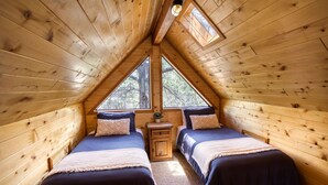 A cozy attic bedroom with two beds, wooden walls, and a skylight. - Cozy cabin w/ loft, private hot tub, near Bison Ranch, sleeps 6 (Overgaard)