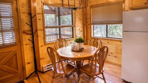 A wooden-paneled room with a round dining table, chairs, a chandelier, and a refrigerator. - Cozy cabin w/ loft, private hot tub, near Bison Ranch, sleeps 6 (Overgaard)
