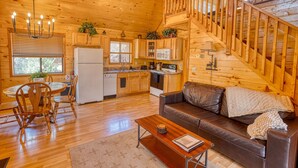 A wooden cabin interior with a dining area, kitchen, and a staircase. - Cozy cabin w/ loft, private hot tub, near Bison Ranch, sleeps 6 (Overgaard)