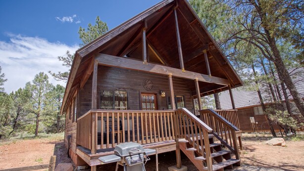 A wooden cabin with a porch, a grill, and a staircase leading to the entrance. - Cozy cabin w/ loft, private hot tub, near Bison Ranch, sleeps 6 (Overgaard)